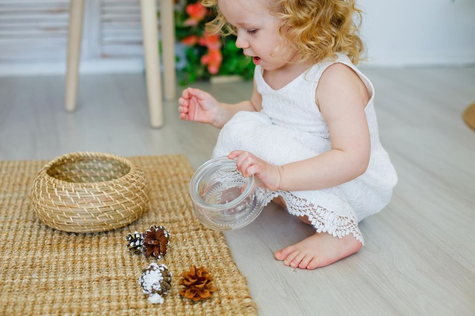Wahrnehmungsspiele zum Selbermachen: Kleinkind hockt vor einem Korb und Tannenzapfen