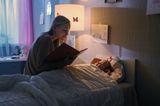 Mutter sitzt am Bett und liest Kind eine Gute-Nacht-Geschichte vor