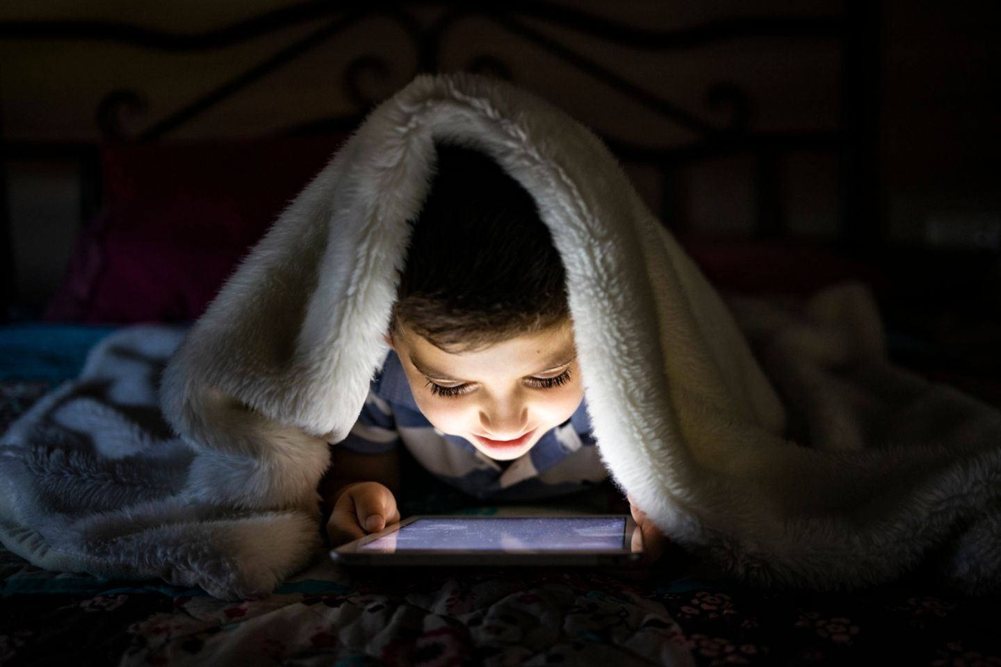 Kind liegt im Bett und schaut auf dem Tablet fern