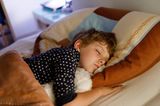 Kind schläft mit eigenem Kuscheltier im Bett