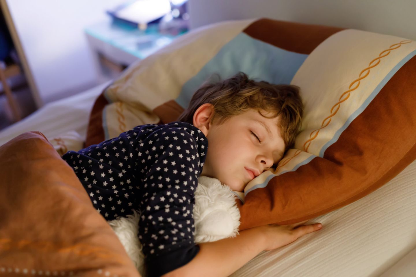 Kind schläft mit eigenem Kuscheltier im Bett