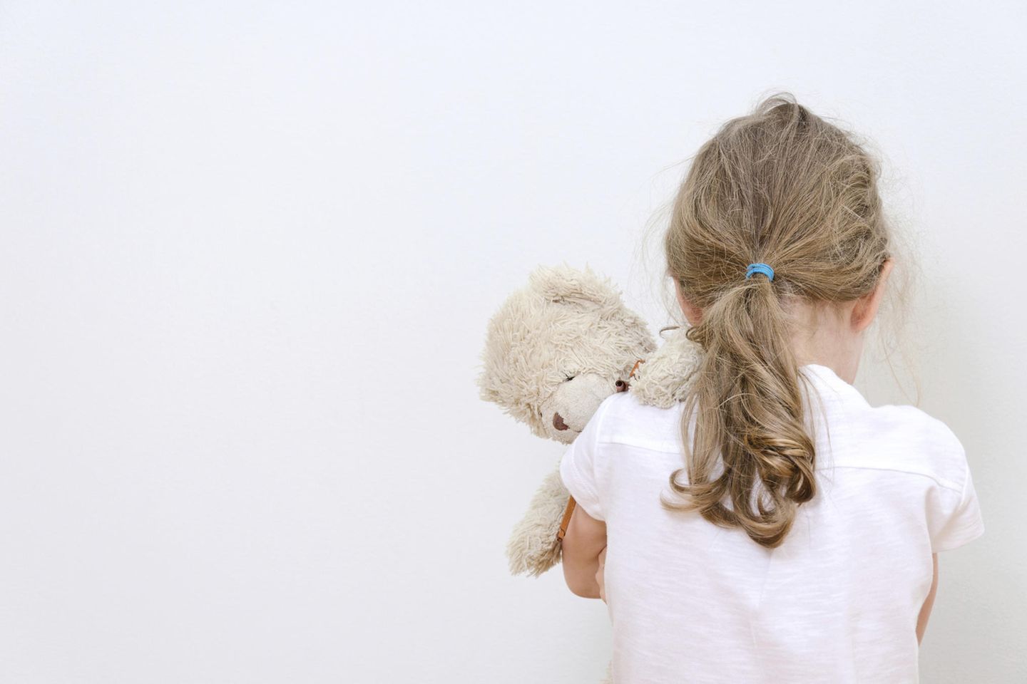 Bettnässen: Rückenansicht eines kleinen Mädchens mit Kuscheltier, das nach unten schaut
