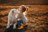 Ein Maedchen spielt draußen mit ihrem weißen Hund