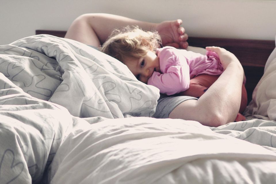 Kleinkind liegt mit Vater im Bett