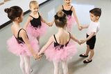 Mädchen tanzen im Kreis und mit Tütü Ballett. Junge reiht sich im Kreis ein