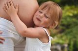 Mädchen kuschelt sich mit Wange an Babybau von Mutter