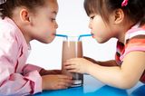 Mädchen trinken aus einen Glas mit 2 Strohhalmen Kakao