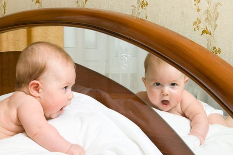 Baby liegt auf dem Bauch im Bett, betrachtet sein Spiegelbild