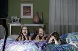 3 Mädchen liegen im Bett, schauen TV, scheinen sich zu fürchten