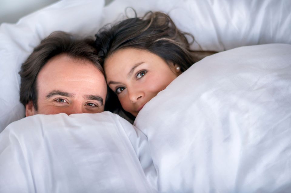 Eisprungrechner: Paar schaut unter der Bettdecke hervor