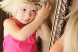 Kleines Mädchen steht mit Schere vorm Spiegel und schneidet sich die Haare