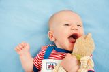 Beschäftigungsideen für dein Baby: Baby liegt lachend auf dem Rücken und hält ein Kuscheltier