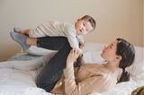 Beschäftigungsideen für dein Baby: Frau liegt auf dem Rücken und lässt Baby auf ihren Beinen fliegen