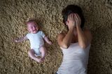 Baby und Frau liegen auf dem Teppich, Frau schlägt Hände vor Gesicht