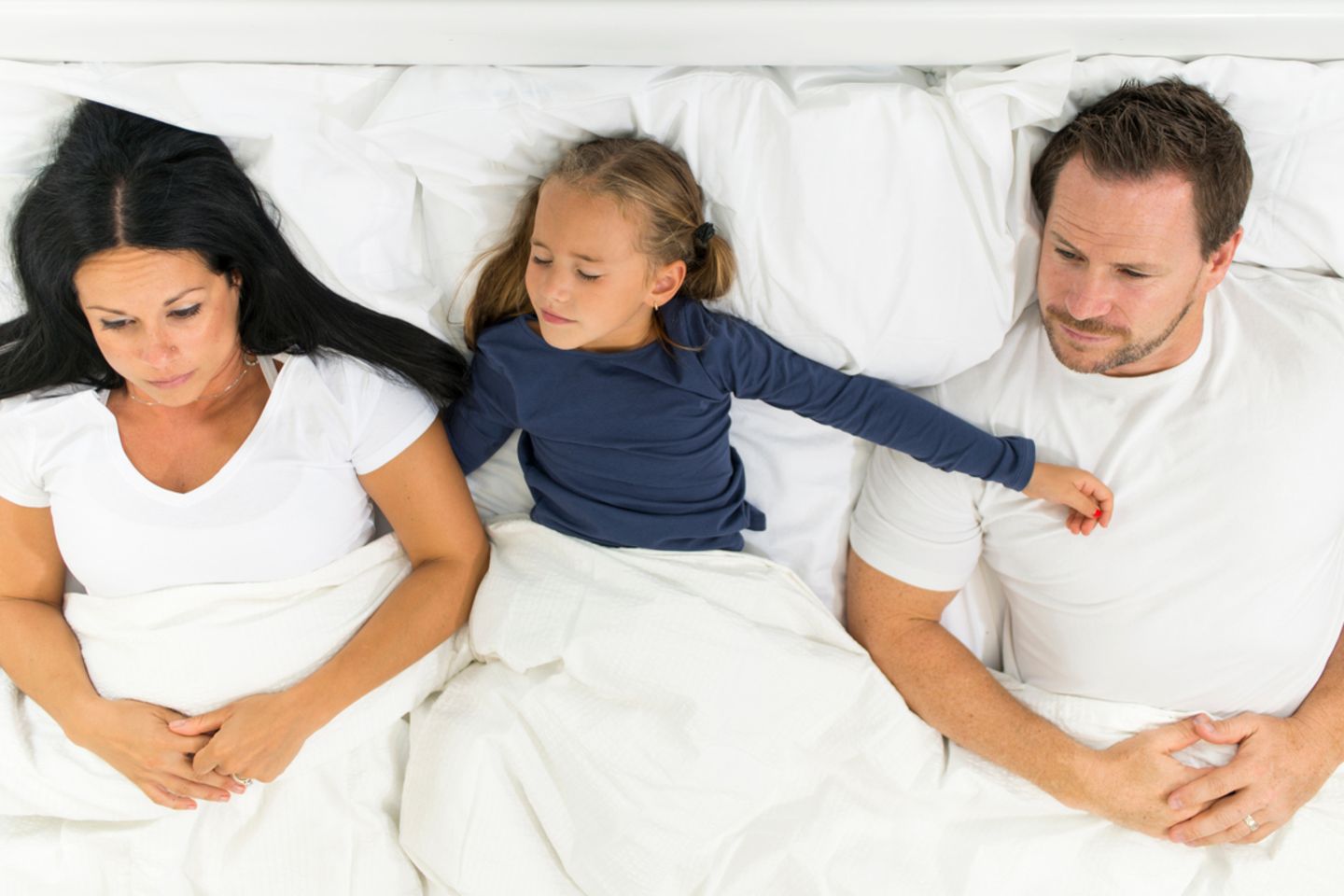 Tochter liegt zwischen den Eltern in der Mitte des Betts