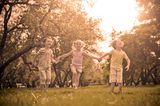 Kinder, die Hand in Hand über eine Wiese laufen
