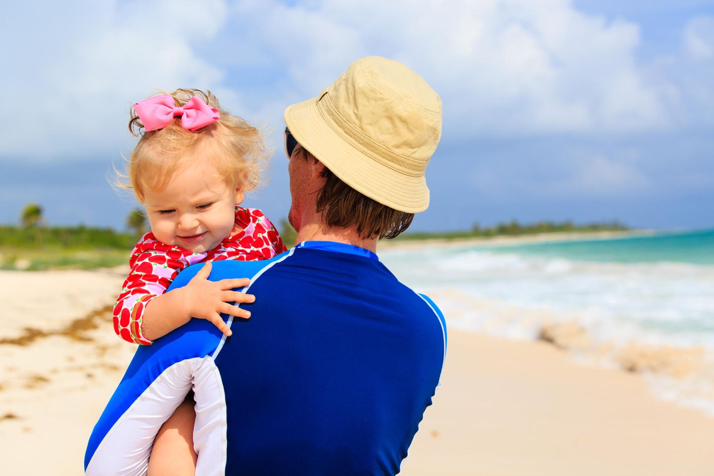 Vater mit Baby am Strand: Gibt es auch schon für Babys Kleidung mit UV-Schutz?
