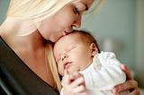 Leichter einschlafen: Junge Frau küsst ihr schlafendes Baby sanft auf den Kopf.