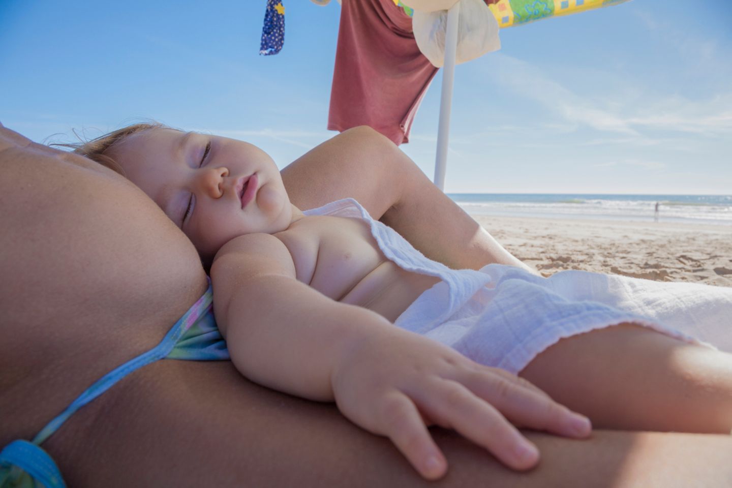 Baby liegt am Strand auf dem Schoß der Mutter und schläft