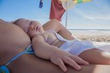 Baby liegt am Strand auf dem Schoß der Mutter und schläft