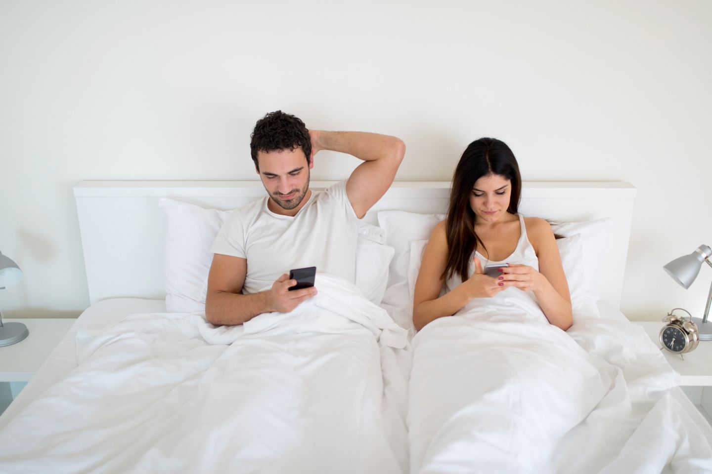 Paar liegt mit Handys im Bett