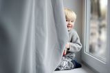 zweijähriger Junge sitzt auf Fensterbank