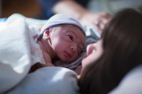 Ein neugeborenes Baby liegt auf der Brust seiner Mutter und blinzelt sie an