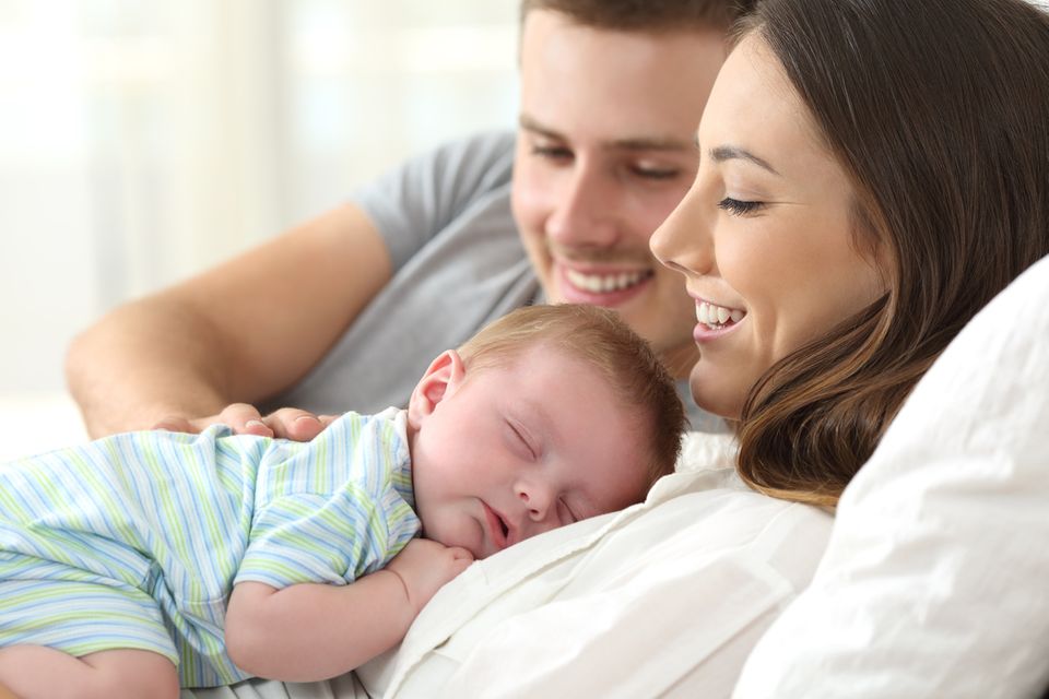 Gehirnentwicklung: Säugling schläft auf Bauch der Mutter, Vater schaut zu