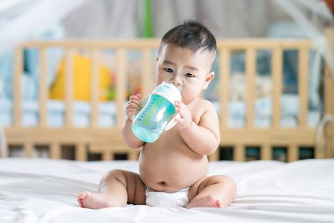 Baby sitzt auf dem Bett und hält eine Wasserflasche