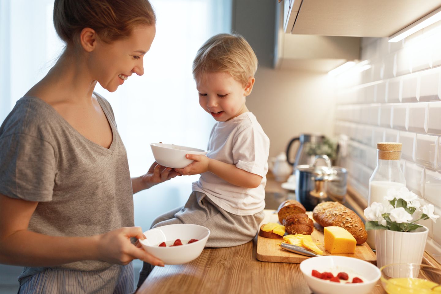 Mutter gibt Kind in der Küche eine Schüssel mit Joghurt und Obst