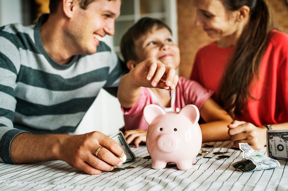 Finanzen: Mutter, Vater und Sohn werfen Geld ins Sparschwein