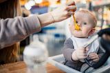 Baby mit Löffel isst Gläschchenmahlzeit