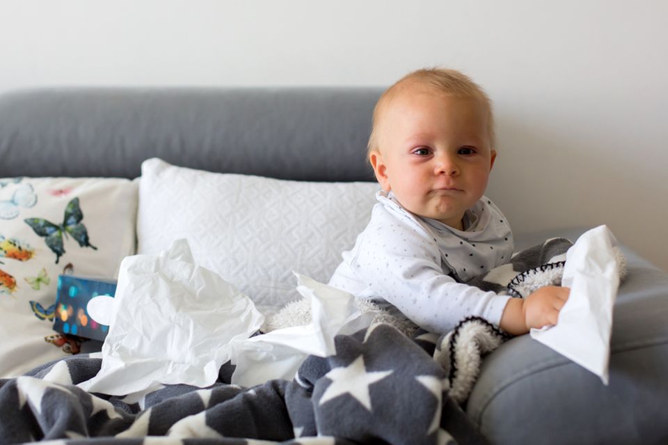 Baby sitzt auf Sofa mit Taschentüchern