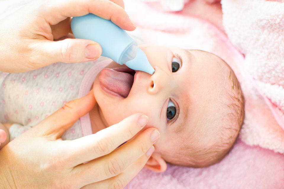 Baby streckt die Zunge raus und wird mit einem Nasensauger behandelt.