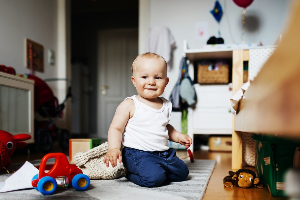 Babyjunge sitzt zwischen seinen Spielsachen