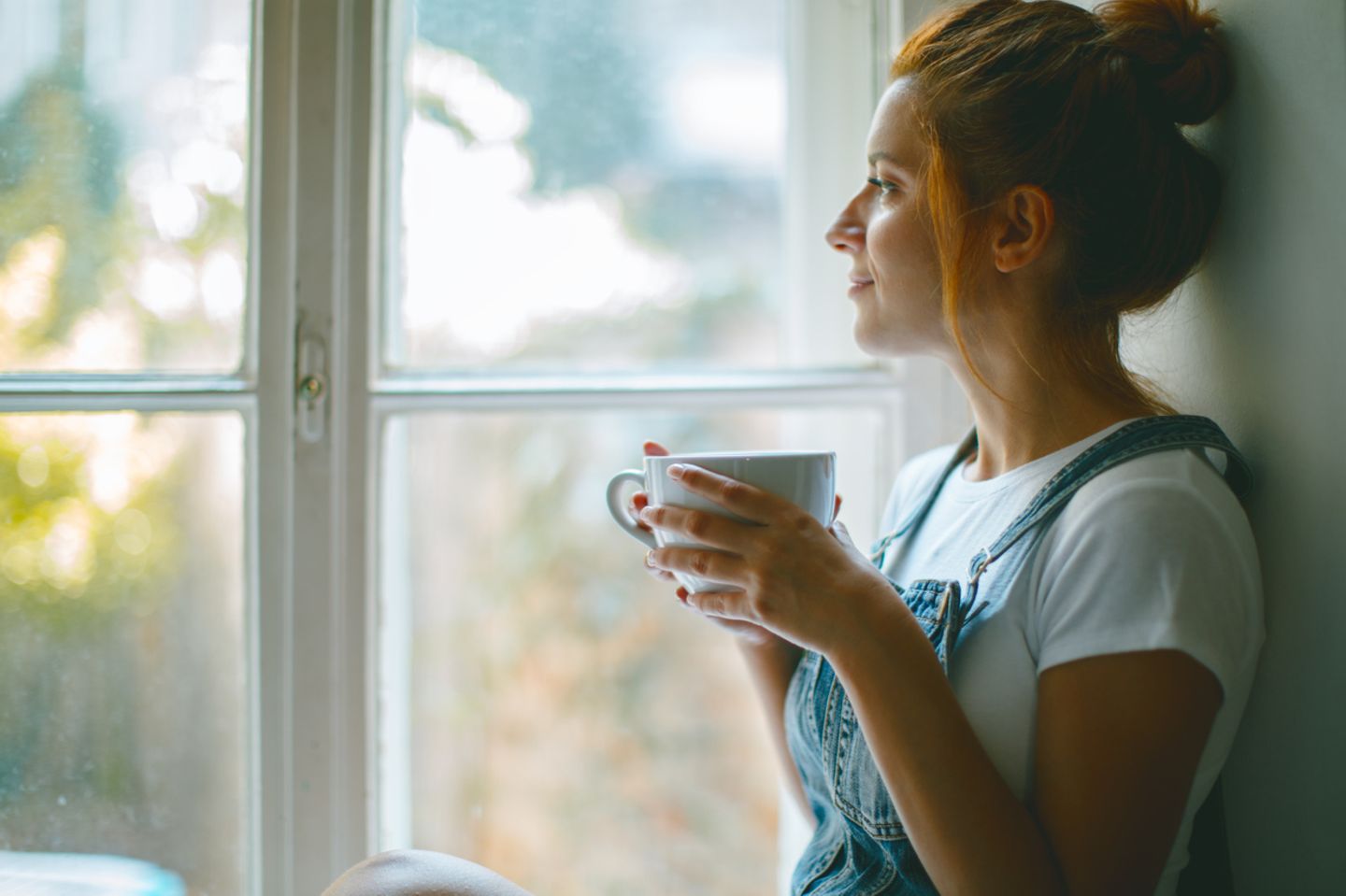 Junge Frau trinkt Kaffee am Fenster