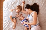Eine Mutter liegt mit ihren zwei kleinen Kindern fröhlich lachend auf dem Bett