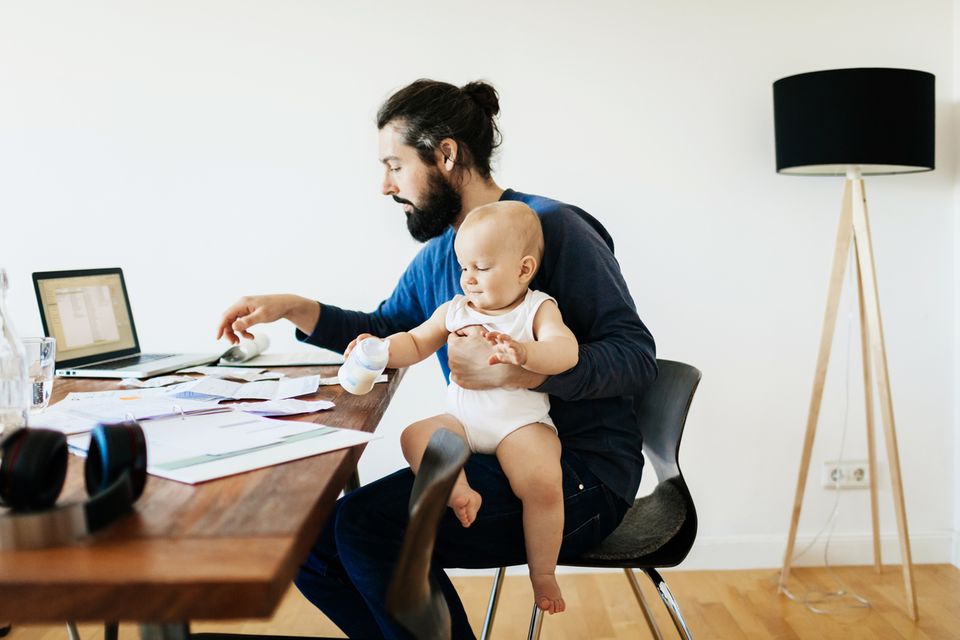 Vater arbeitet im Home Office und hat dabei sein Baby auf dem Schoß