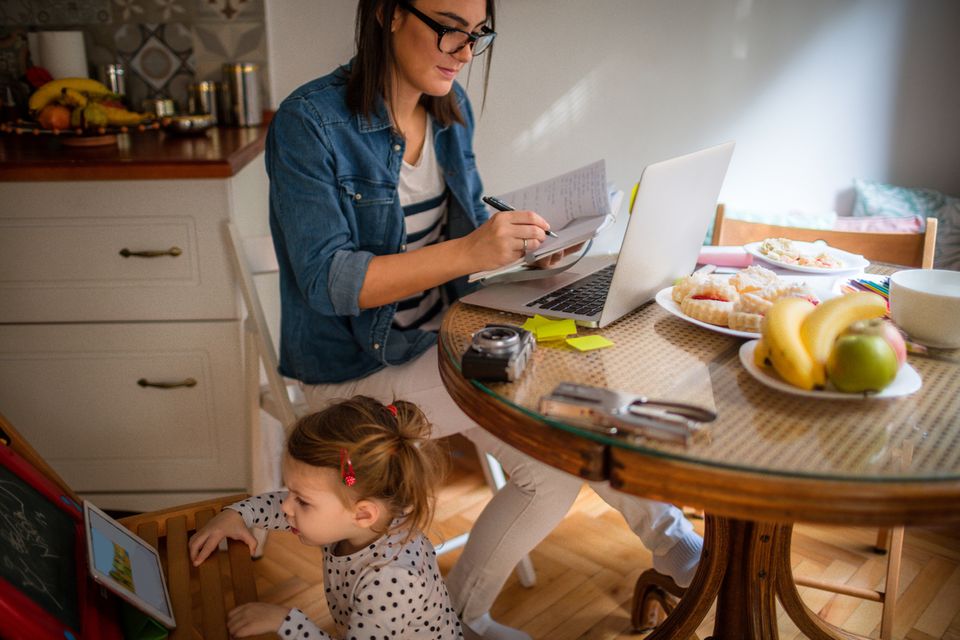 Mutter arbeitet am Laptop im Home Office, die Tochter spielt am Tablet Mutter arbeitet am Laptop im Home Office, die Tochter spielt am Tablet