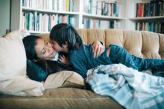 Mutter liegt auf Sofa und wird von Sohn geküsst