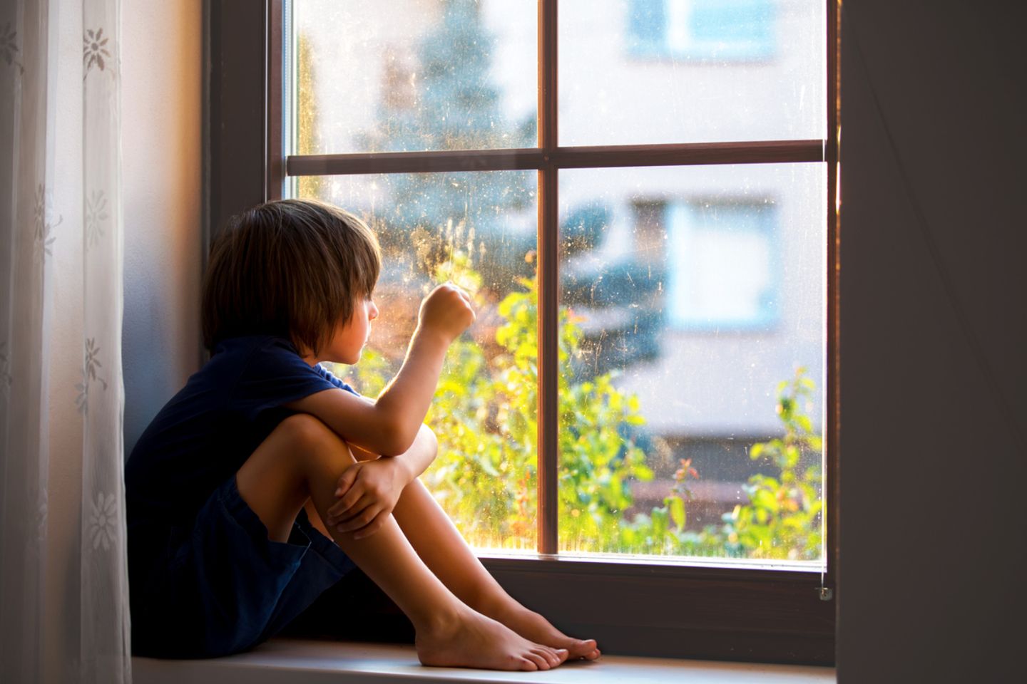 Ein Junge schaut sehnsüchtig aus dem Fenster und versucht mit dem Social Distancing klarzukommen.