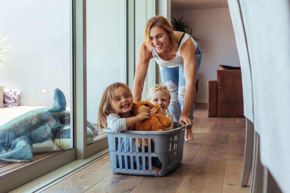 Eine Mutter spielt drinnen mit ihren zwei Kindern und einem Wäschekorb