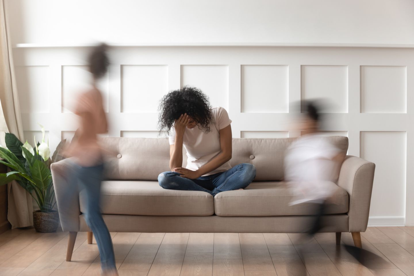Eine gestresste Mutter sitzt auf dem Sofa während ihre zwei Kinder wild toben