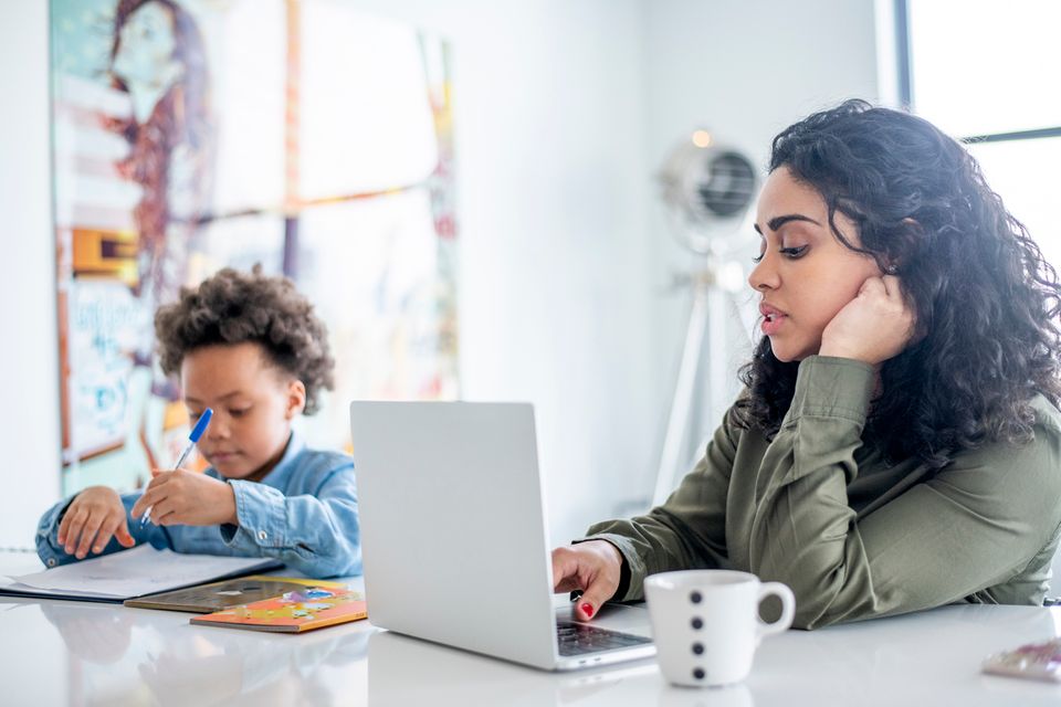Mutter stellt Elterngeldantrag und arbeitet am Laptop, Kind sitzt daneben