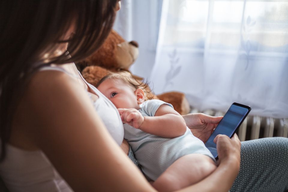 Eine Mutter stillt ihr Baby und spielt dabei mit dem Handy