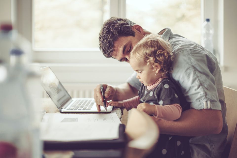 Ein Vater hat seine Tochter auf dem Schoß und arbeitet am Laptop