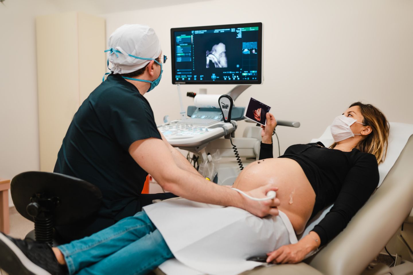 Schwangere Frau mit Mundschutz beobachtet ihr Baby auf dem Ultraschall