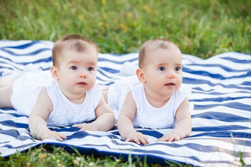 Zwillinge-liegen-auf-einer-Decke-im-Gras