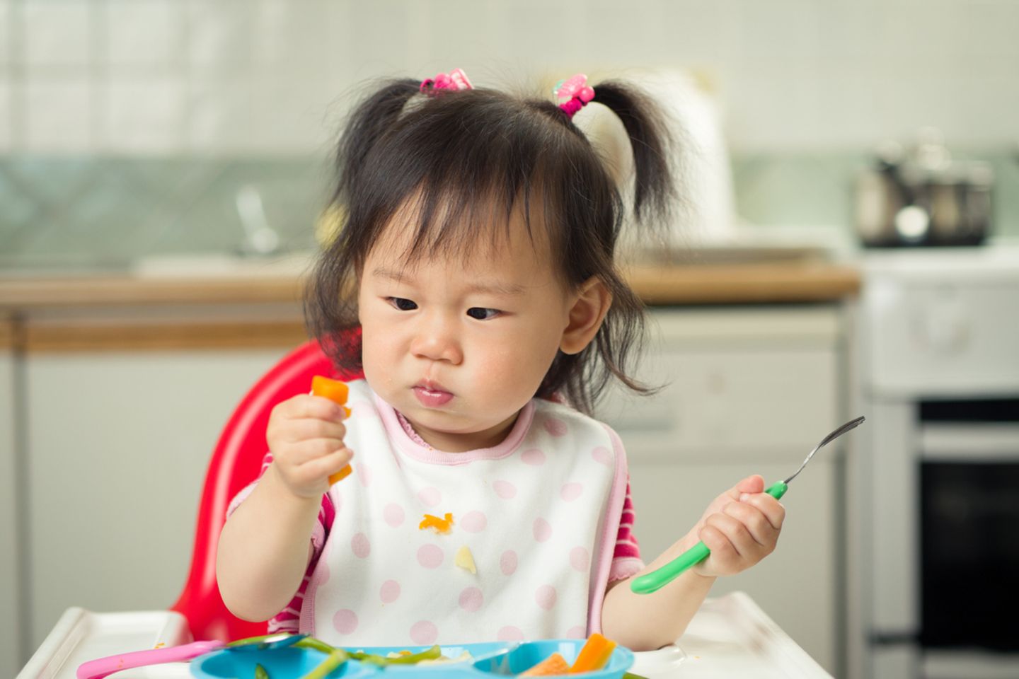 Kleines asiatisches Mädchen isst Gemüsestückchen
