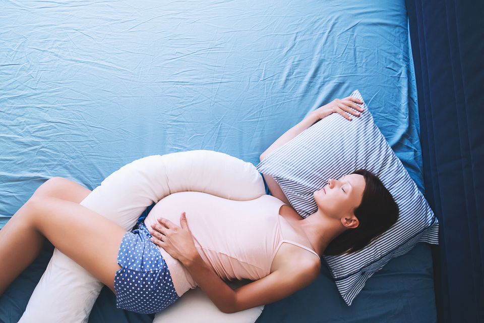 Schwangere-liegt-mit-Kissen-zwischen-den-Beinen-im-Bet Schwangere-liegt-mit-Kissen-zwischen-den-Beinen-im-Bet
